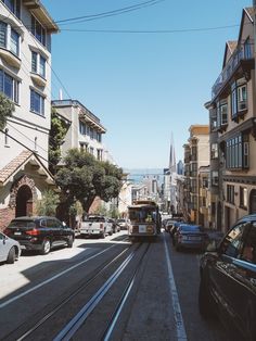 cars are driving down the street in front of buildings and a cable car is on the road