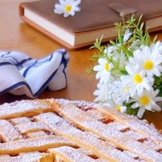 a table topped with a cake covered in powdered sugar next to a bouquet of daisies