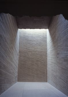 an empty room with light coming in from the ceiling and stone blocks on the walls