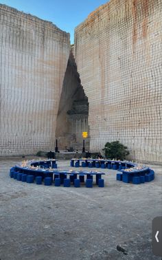 an outdoor seating area in front of a large stone structure with blue seats around it