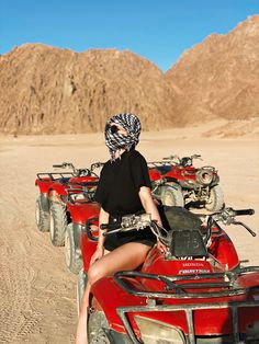 a woman riding on the back of an atv in the middle of desert with mountains behind her