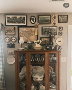 a china cabinet with plates and pictures on the wall