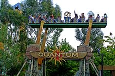 an amusement park ride with people riding on the roller coasters and trees in the background