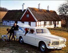 three people are standing on the hood of a car with two dogs in front of it