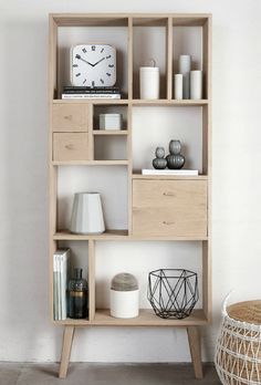 a wooden shelf with various items on it and a basket next to it in front of a white wall