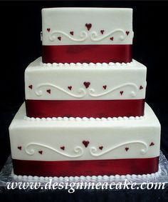 a three tiered wedding cake with hearts on the top and red ribbon at the bottom