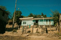 a blue house sitting on the side of a dirt road next to a fence and trees