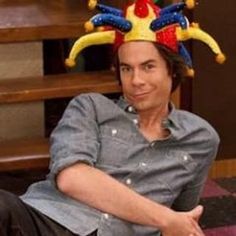 a man sitting on the floor wearing a funny hat that looks like a clown's head