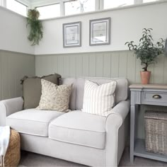 a white couch sitting in a living room next to a table with two potted plants on it