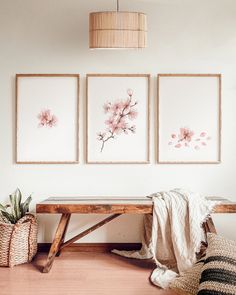 three pink flowers are hanging on the wall above a wooden bench in front of a wicker basket