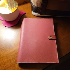 a pink notebook sitting on top of a wooden table next to a cup and vase