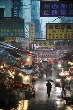 a person with an umbrella walking down a street at night in the rain, surrounded by buildings and signs