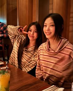 two young women sitting at a table with food and drinks in front of them, posing for the camera