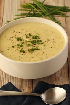 a white bowl filled with soup on top of a wooden table next to a spoon