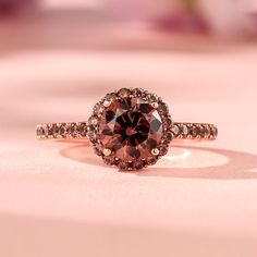 a pink diamond ring sitting on top of a white surface with flowers in the background