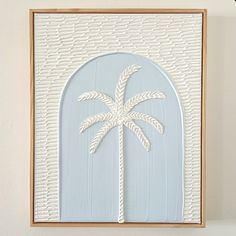 a white palm tree on a light blue background in a wooden frame hanging on a wall