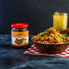 a wooden bowl filled with noodles next to a jar of mustard