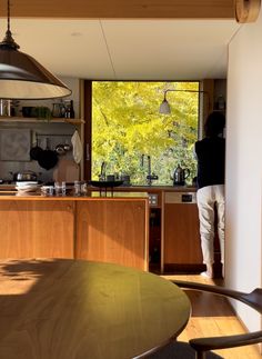 a person standing in a kitchen next to a wooden table and chairs with an open window