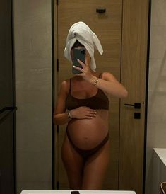 a pregnant woman taking a selfie in the bathroom with her cell phone and towel over her head