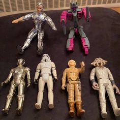 five toy action figures sitting on top of a black cloth covered table next to each other