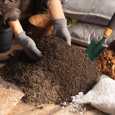 a person shoveling dirt into a pile of mulch next to a potted plant