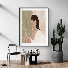 a woman holding a plant in her hand next to a chair and table with a potted cacti