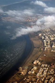 an aerial view of a city and the ocean with clouds in the sky above it