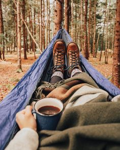 a person laying in a hammock holding a cup of coffee