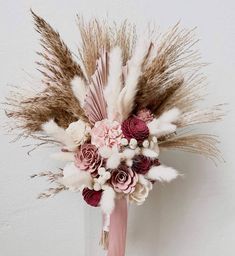 a vase filled with flowers and feathers on top of a white table next to a wall