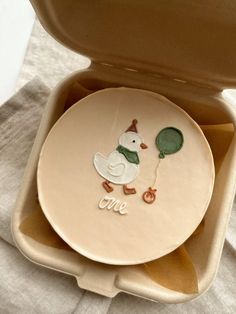 a ceramic plate with a duck on it in a box that says me and is holding a balloon