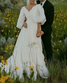 a bride and groom standing in a field with wildflowers