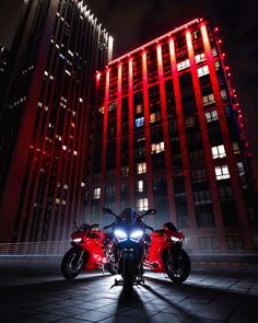 two motorcycles parked in front of a tall building at night with red lights on them