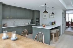 a kitchen with green cabinets and white counter tops, wooden table in front of the island