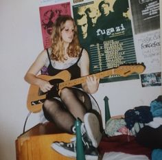 a young woman sitting on top of a bed holding a guitar in front of her