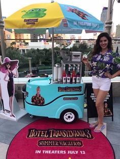 a woman standing next to a blue food truck on top of a red area rug