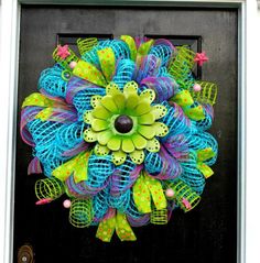 a blue and green mesh wreath with flowers hanging on a black front door, decorated with polka dots