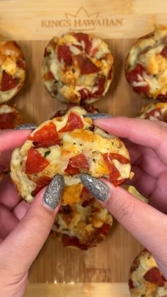 two hands holding small pizzas with toppings on them in front of a wooden board