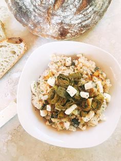 a white bowl filled with food next to a loaf of bread on top of a table