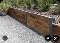 an image of a wooden fence in the middle of a gravel area with trees and bushes behind it