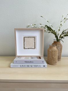 two vases with flowers are sitting on a table next to books and a book