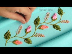 a hand is stitching flowers on a blue fabric with green leaves and pink flowers