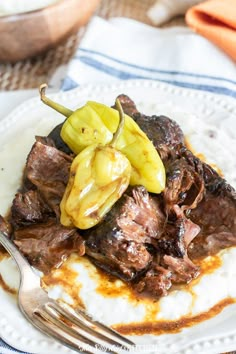 a close up of a plate of food with meat and peppers on it, next to a fork