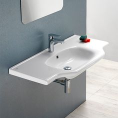 a white bathroom sink sitting next to a wall mounted mirror on the side of a gray wall