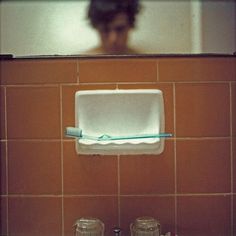 a bathroom sink with a toothbrush and soap dispenser on the wall