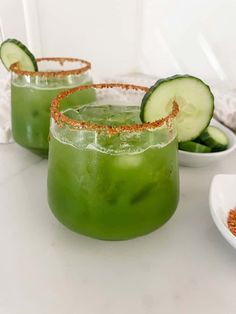 two glasses filled with green liquid and cucumber garnished with red glitter