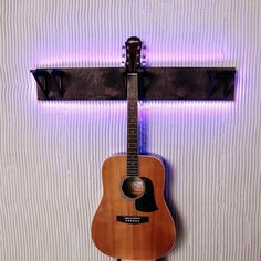 an acoustic guitar hanging on a wall with a purple light behind it in front of a white background