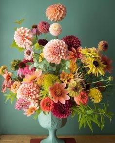 a blue vase filled with lots of colorful flowers on top of a wooden table next to a green wall