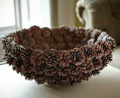 a bowl filled with pine cones sitting on top of a white table next to a chair