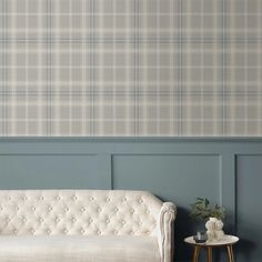 a white couch sitting in front of a wall with blue and gray plaid pattern on it