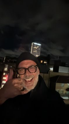 a man with glasses and a hat on talking on a cell phone in front of a cityscape